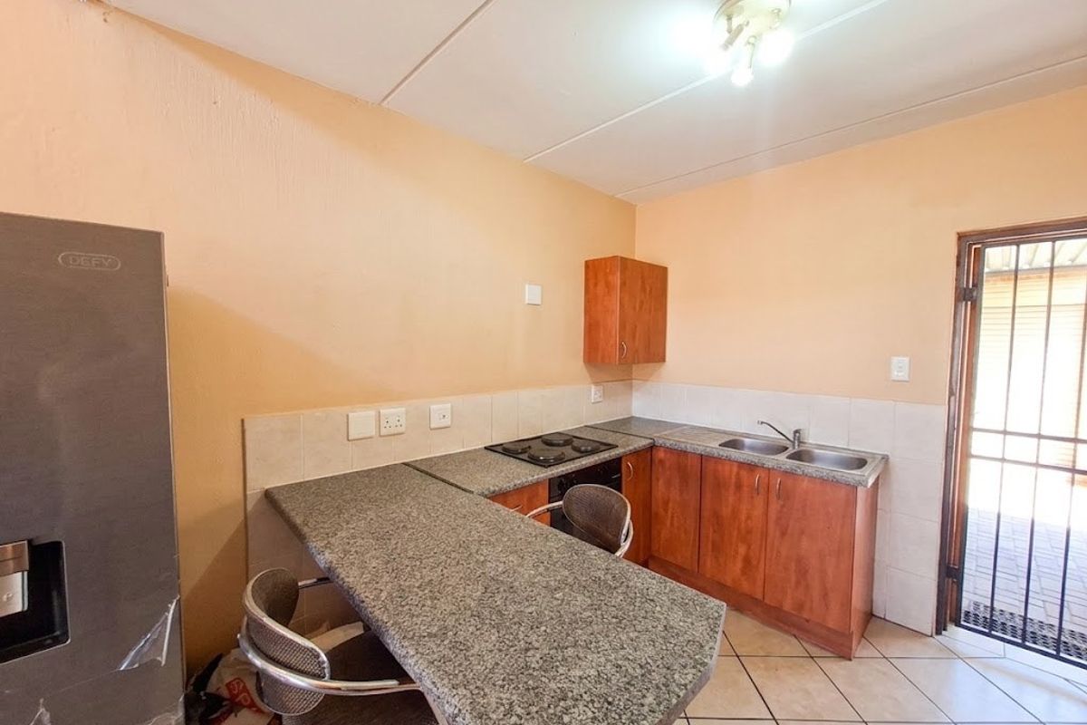 Functional kitchen featuring granite countertops, built-in hob, double sink, and laminate cabinetry with direct access to an outdoor area.