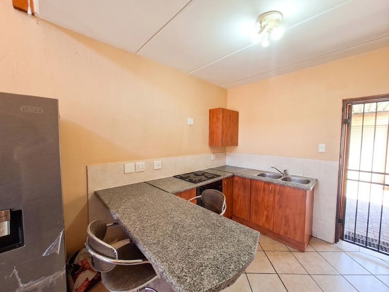 Functional kitchen featuring granite countertops, built-in hob, double sink, and laminate cabinetry with direct access to an outdoor area.