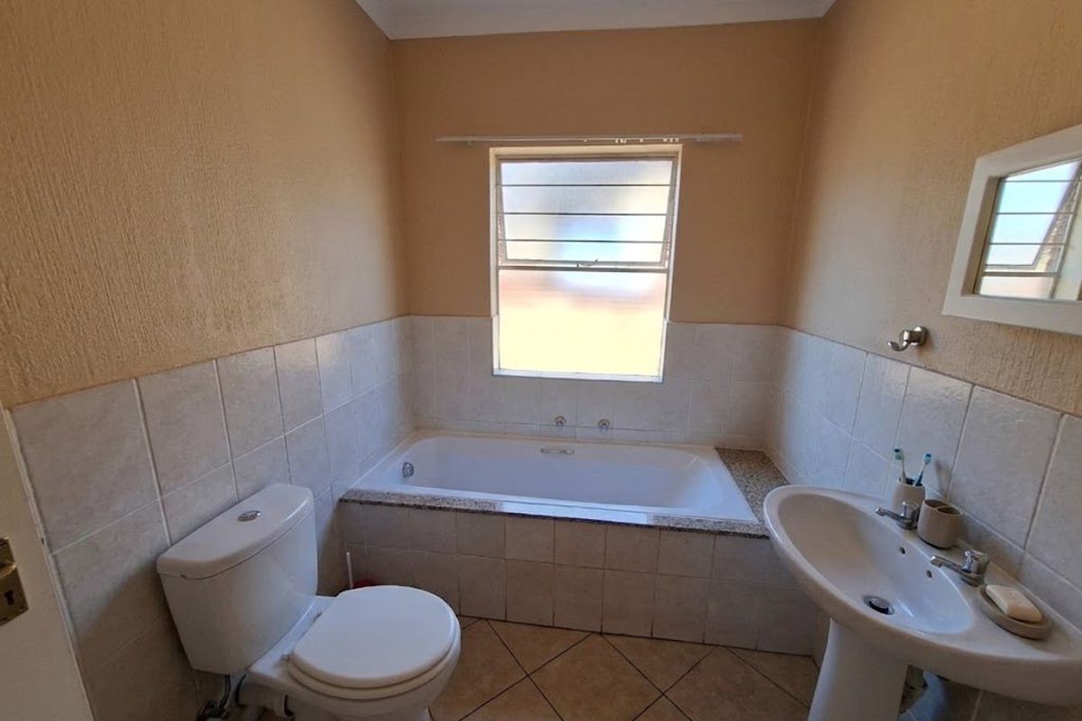 A functional bathroom featuring a built-in bathtub, pedestal basin, and toilet with neutral wall paint and tiled flooring.