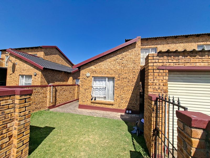 Rear view of a face brick townhouse featuring a small private garden, paved patio area, and secure gated access to the garage.