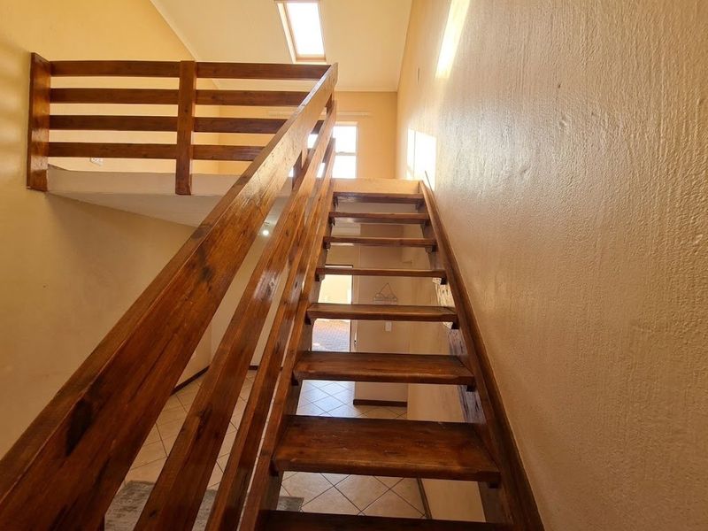 A staircase with a wooden balustrade leading to an upper mezzanine level, featuring a skylight and tiled flooring.