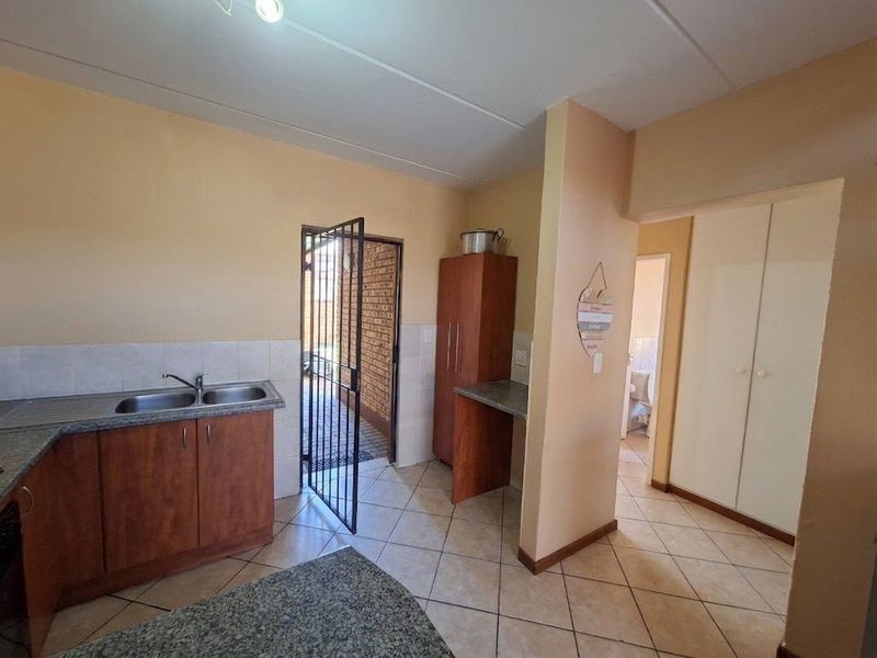Kitchen area featuring laminate cabinetry, double bowl sink, tiled flooring, and direct access to an exterior security gate.