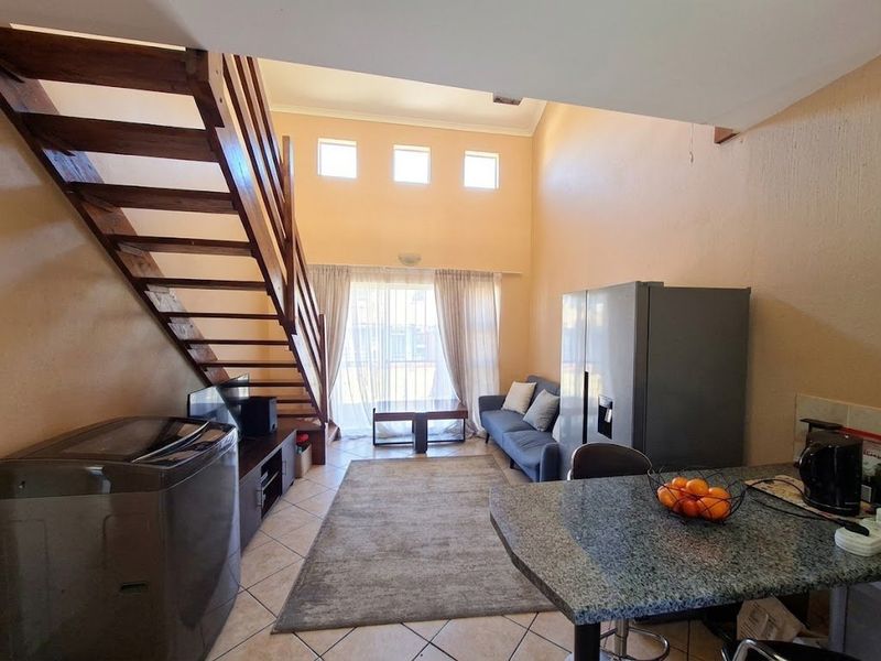 Open-plan living area featuring a wooden staircase, high ceilings, and a kitchen with granite countertops, creating a spacious and functional layout.