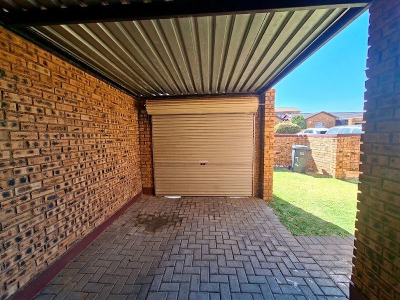 A covered carport area featuring brick walls, a roller shutter door, and paved flooring, providing secure parking space.