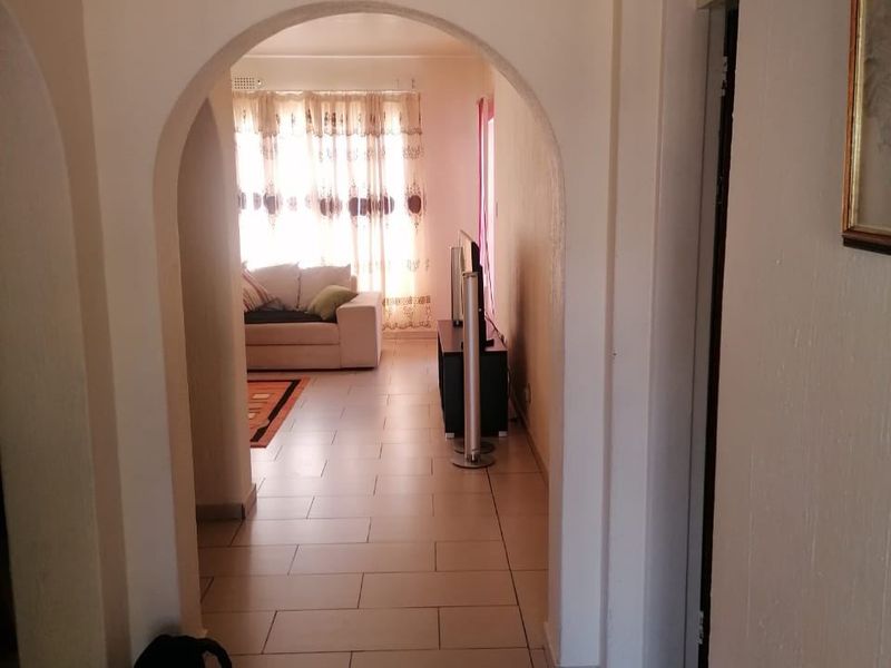 A view through an arched doorway into a living area, featuring neutral tiled flooring and a bright, naturally lit space.