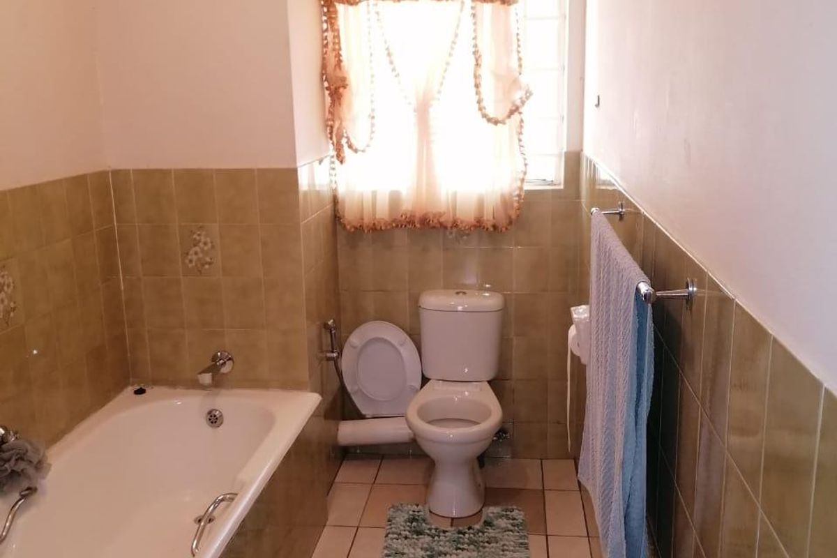 A functional bathroom featuring a bathtub, toilet, and tiled finishes, offering a classic layout with natural light from the window.