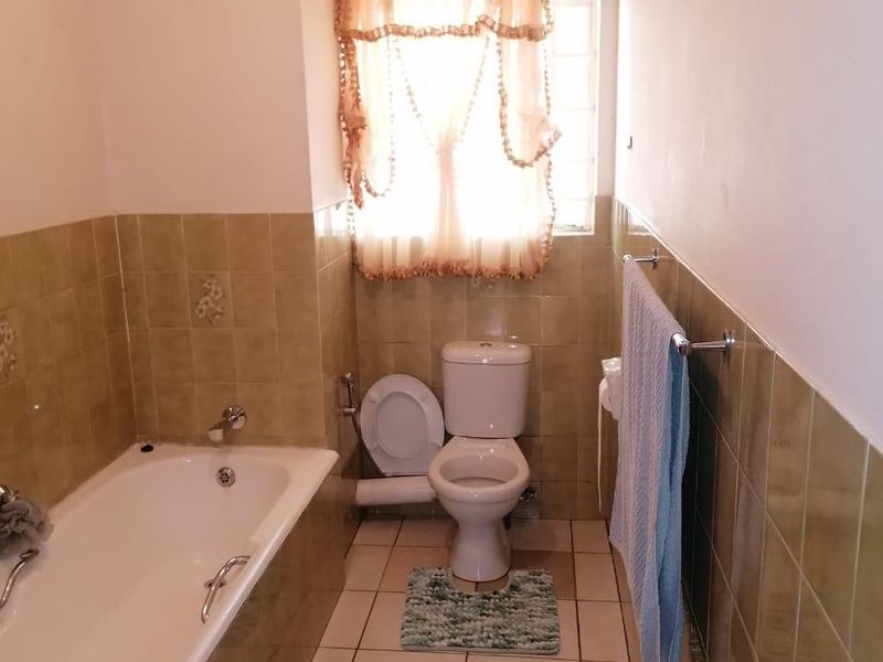 A functional bathroom featuring a bathtub, toilet, and tiled finishes, offering a classic layout with natural light from the window.
