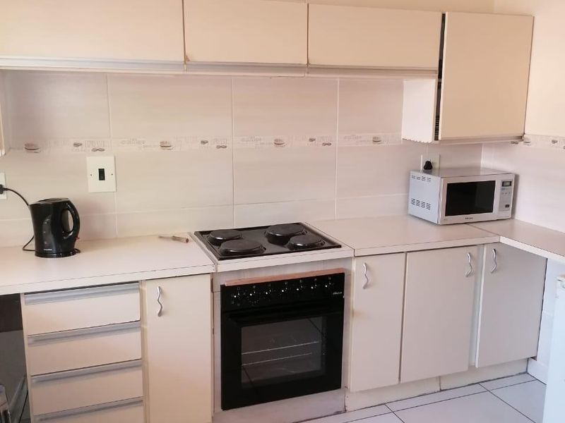 A functional kitchen featuring built-in cabinetry, a tiled backsplash, electric hob, and oven with tiled flooring throughout.