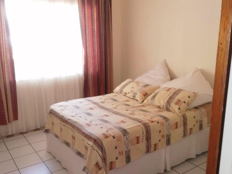 A functional bedroom featuring tiled flooring and a large window with curtains, providing a simple and practical living space.