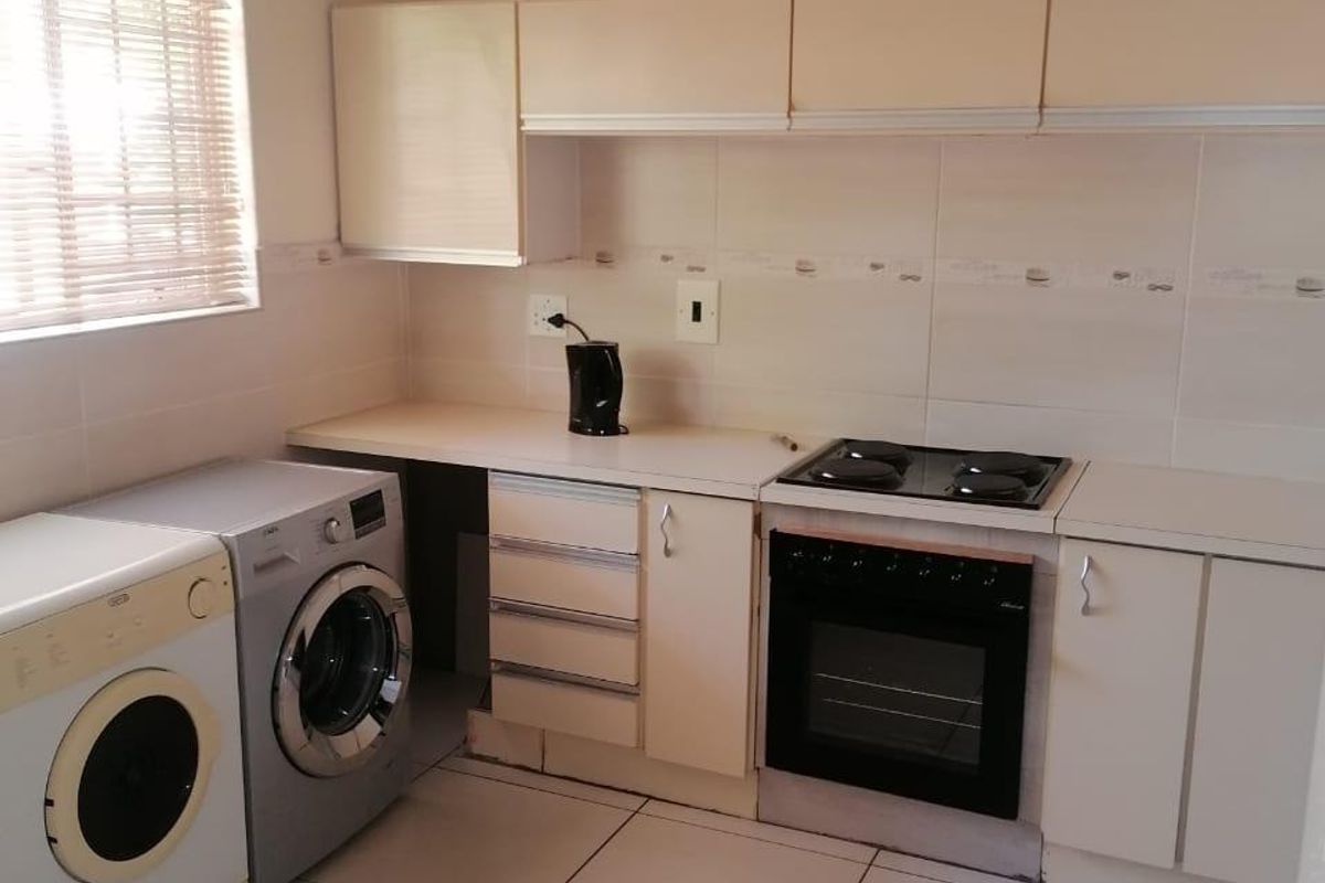 A functional kitchen featuring tiled flooring, built-in cabinetry, a hob, and an oven, with space for laundry appliances.