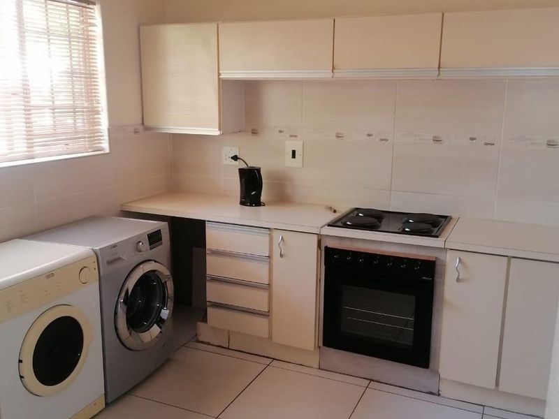 A functional kitchen featuring tiled flooring, built-in cabinetry, a hob, and an oven, with space for laundry appliances.
