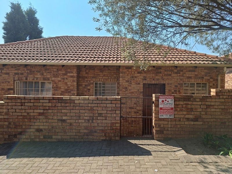 Front exterior view of a face brick townhouse featuring a tiled roof, paved driveway, and secure boundary wall with a metal gate.