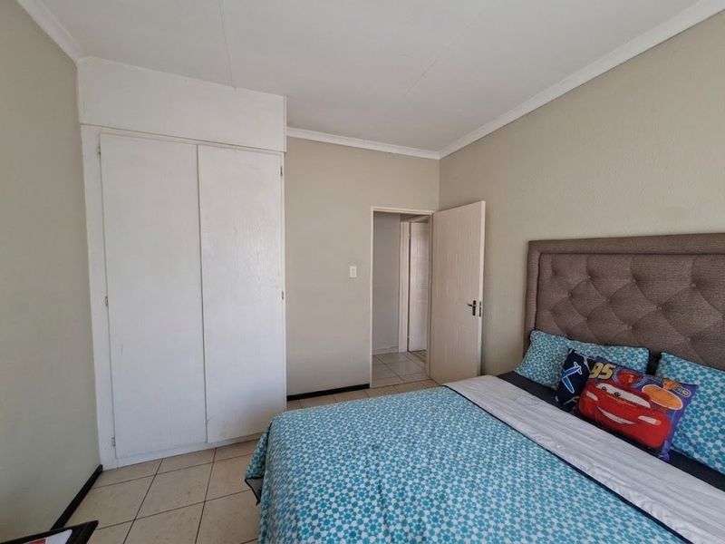 A functional bedroom featuring tiled flooring, a built-in wardrobe, and neutral wall finishes, providing a clean and simple living space.
