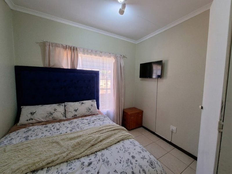 A functional bedroom featuring tiled flooring, neutral wall finishes, and a wall-mounted television point.