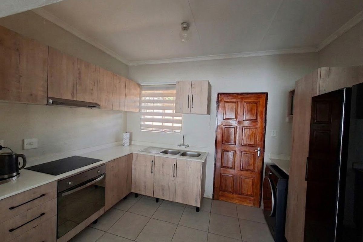 A functional kitchen featuring light wood-look cabinetry, laminate countertops, a built-in oven and hob, and tiled flooring with direct access to an exterior door.