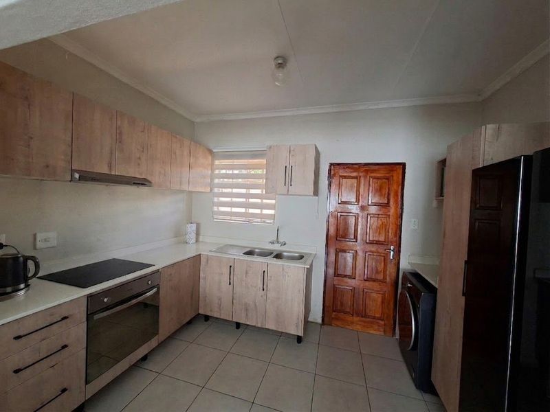 A functional kitchen featuring light wood-look cabinetry, laminate countertops, a built-in oven and hob, and tiled flooring with direct access to an exterior door.