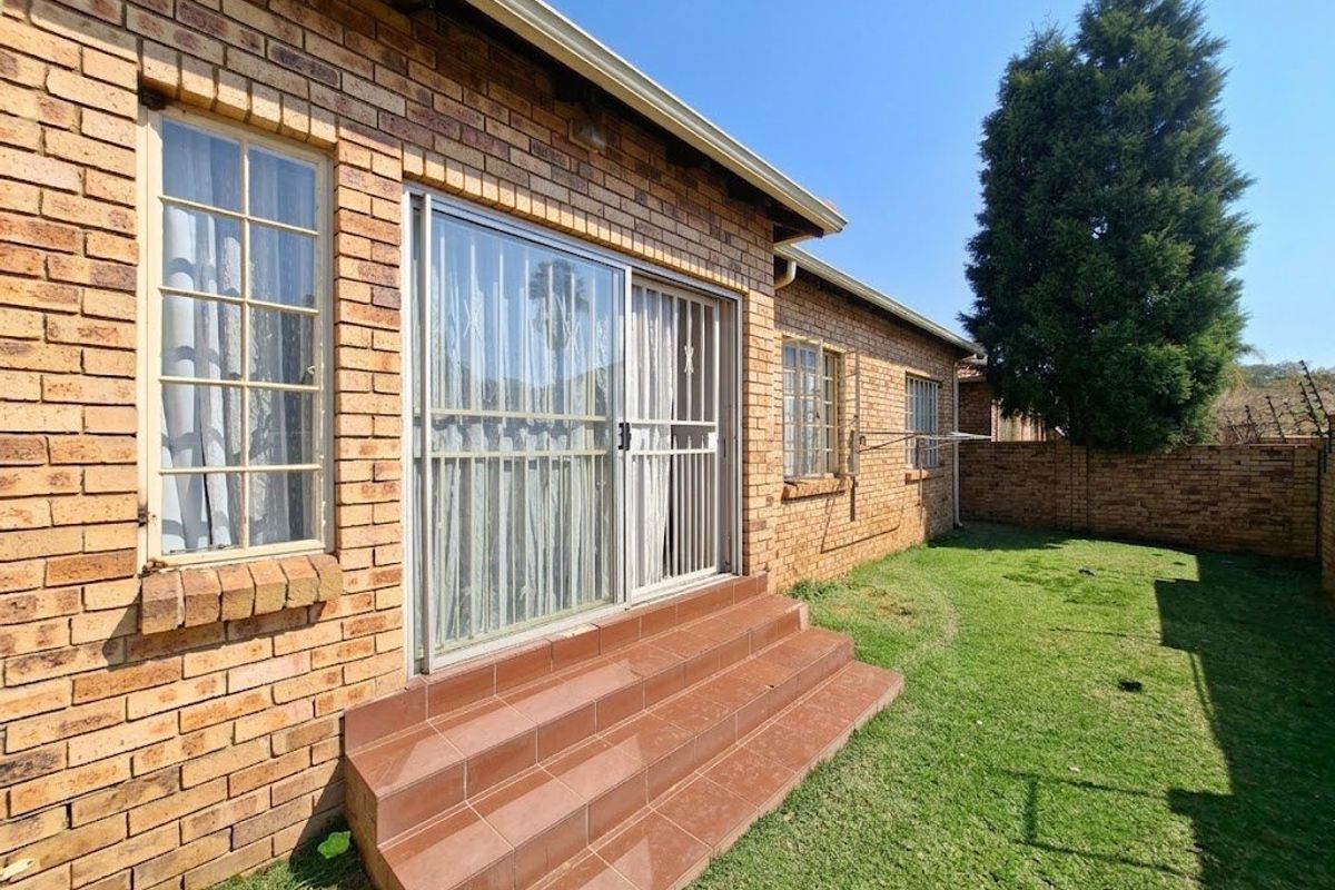 Rear view of the townhouse featuring a face brick facade, sliding door access with tiled steps, and a private lawn area.