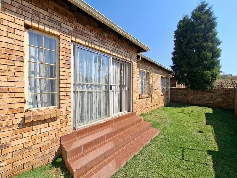 Rear view of the townhouse featuring a face brick facade, sliding door access with tiled steps, and a private lawn area.