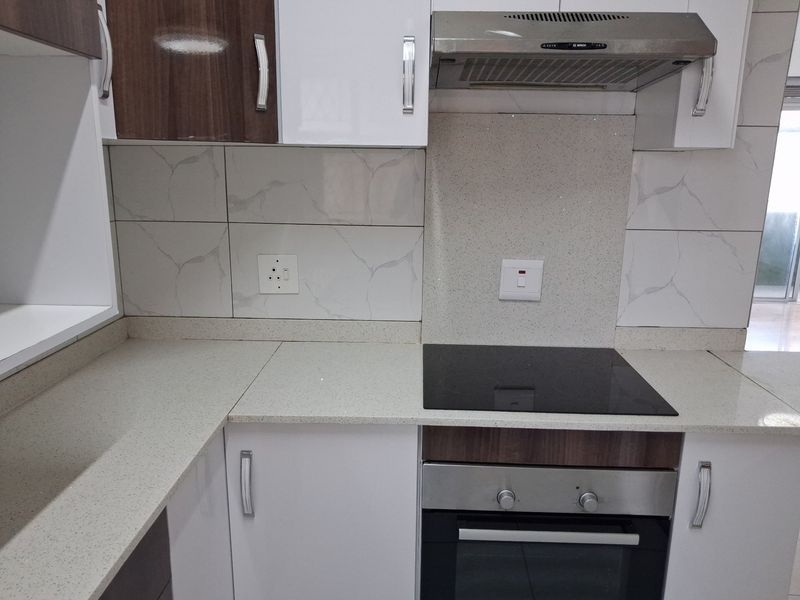 Modern kitchen featuring white and wood-tone cabinetry, stone countertops, a built-in electric oven, hob, and stainless steel extractor fan.