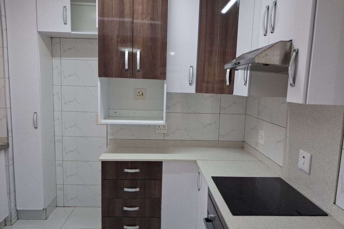 Modern kitchen featuring two-tone cabinetry, stone countertops, integrated electric hob, oven, and extractor fan with a clean tiled backsplash.