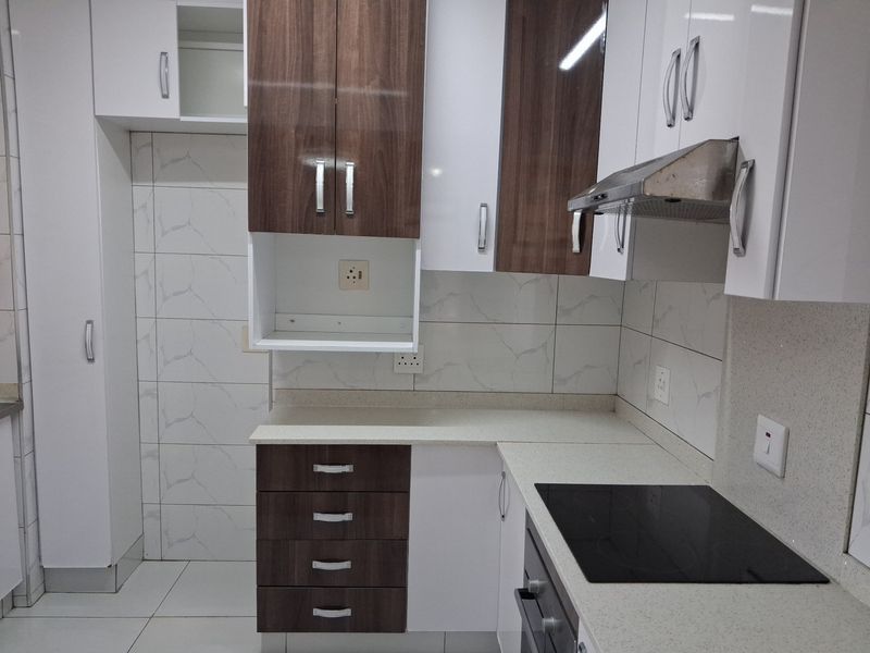Modern kitchen featuring two-tone cabinetry, stone countertops, integrated electric hob, oven, and extractor fan with a clean tiled backsplash.
