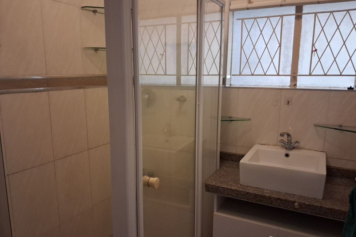 A functional bathroom featuring a shower enclosure, a modern vessel basin on a stone countertop, and built-in vanity storage with tiled wall finishes.