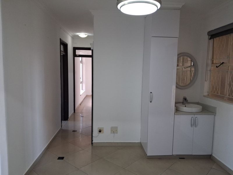 A clean, tiled hallway featuring a built-in vanity with basin and storage cupboard, leading to adjacent rooms with security gate access.