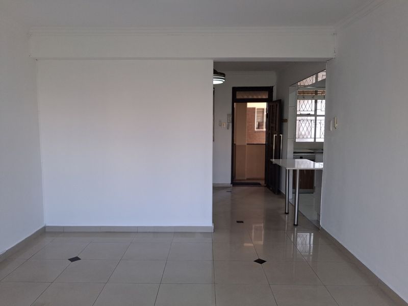An empty open-plan living area featuring tiled flooring, a built-in breakfast counter, and a security gate leading to the entrance.