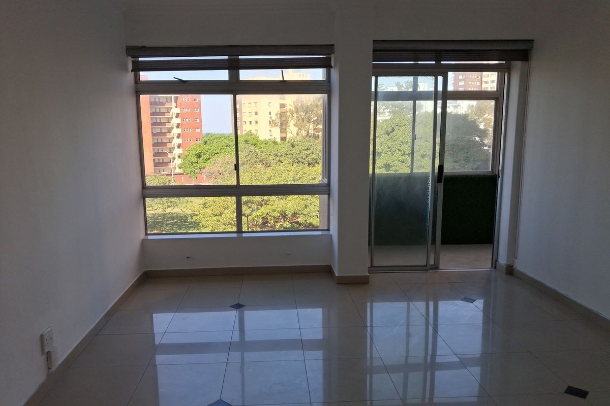 A bright, empty living area featuring polished tiled floors, large windows, and a sliding glass door leading to an outdoor space.