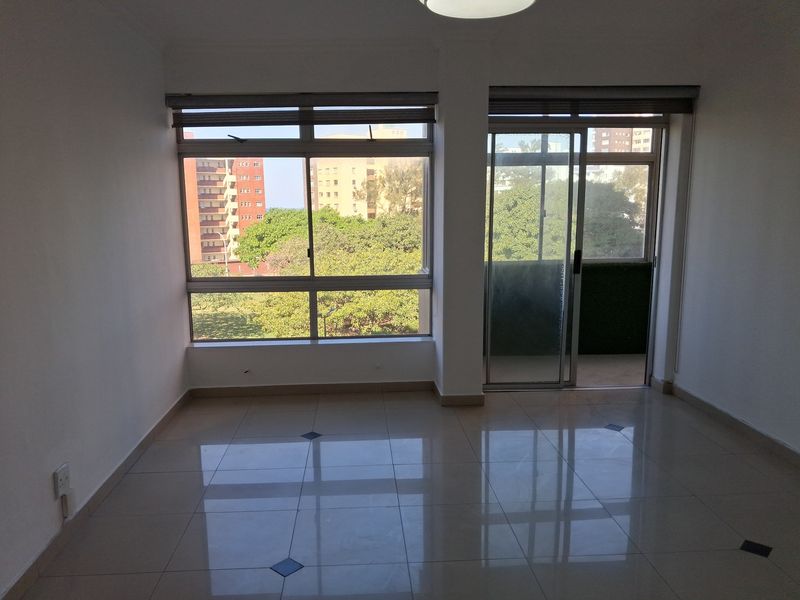 A bright, empty living area featuring polished tiled floors, large windows, and a sliding glass door leading to an outdoor space.