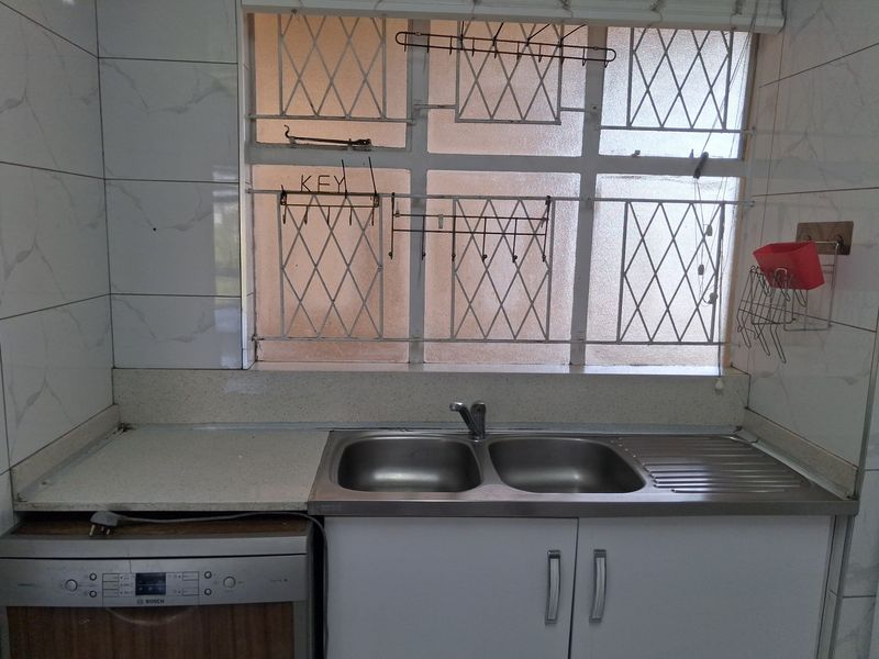 A functional kitchen area featuring a double stainless steel sink, stone countertops, tiled backsplash, and built-in cabinetry with an integrated dishwasher.