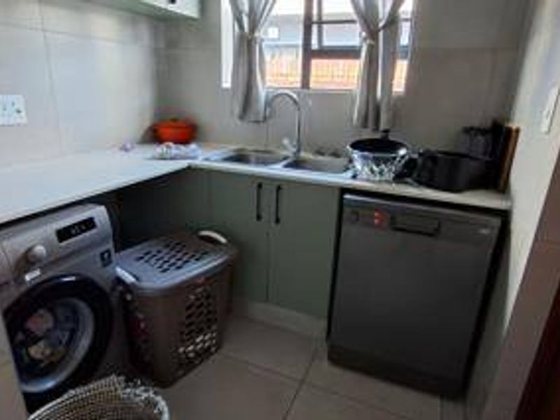 A functional scullery area featuring built-in cabinetry, a double sink with mixer tap, and dedicated plumbing connections for laundry and dishwashing appliances.