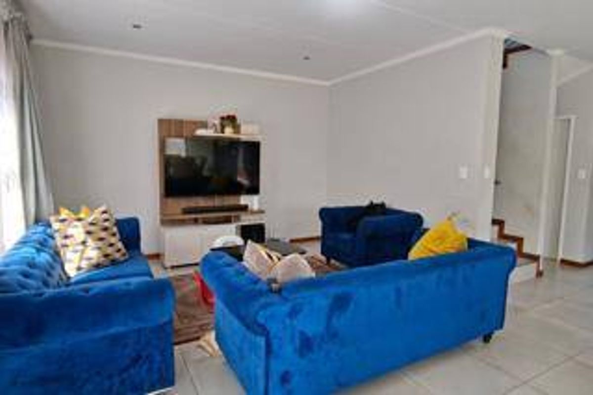 A well-lit living room featuring neutral tiled flooring, recessed downlighting, and an open-plan layout with access to an internal staircase.