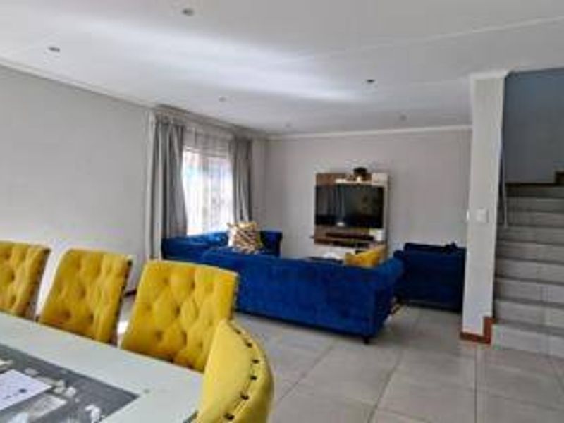 Open-plan living and dining area featuring tiled flooring, recessed lighting, and a staircase leading to the upper level.