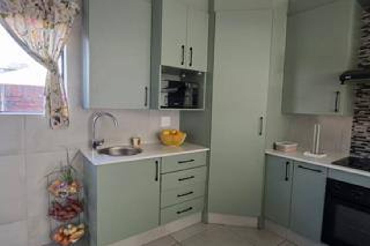Modern kitchen featuring sage green cabinetry, white countertops, built-in oven, hob, extractor fan, and tiled finishes.