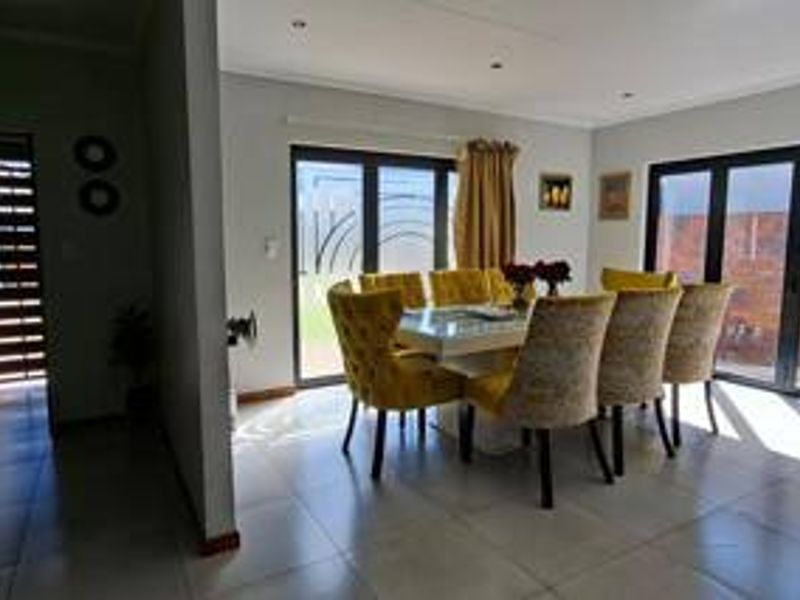 A bright dining area featuring large aluminium sliding doors providing natural light and access to the outdoor space, complemented by modern tiled flooring.