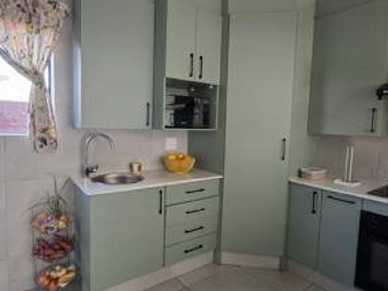Modern kitchen featuring sage green cabinetry, white countertops, built-in oven, hob, extractor fan, and tiled finishes.