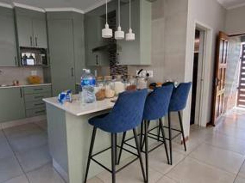 Modern kitchen featuring sage green cabinetry, a central island with breakfast bar seating, stone countertops, and tiled flooring.