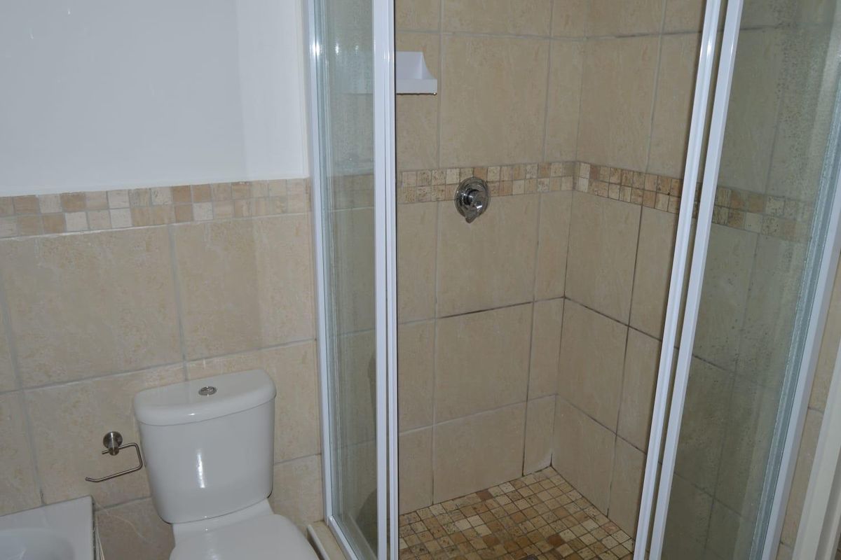 A functional bathroom featuring a glass-enclosed shower with tiled walls and a standard toilet, presenting a dated but well-maintained layout.