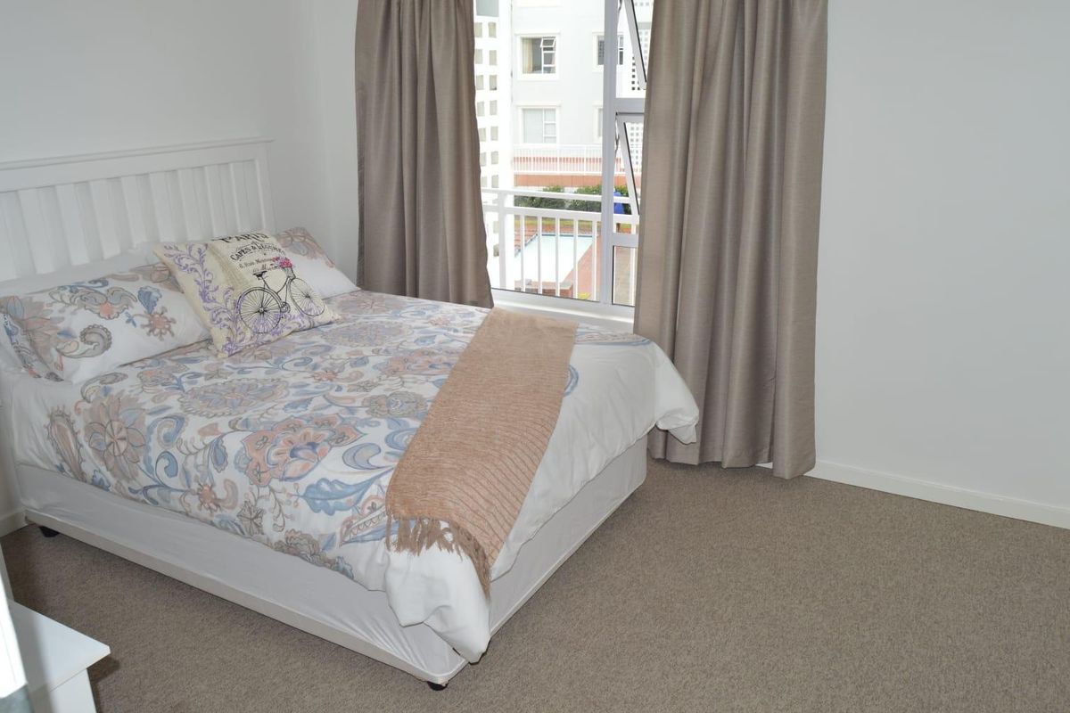 A well-maintained bedroom featuring neutral carpeting, a large window with natural light, and direct access to a balcony.