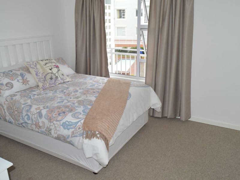 A well-maintained bedroom featuring neutral carpeting, a large window with natural light, and direct access to a balcony.