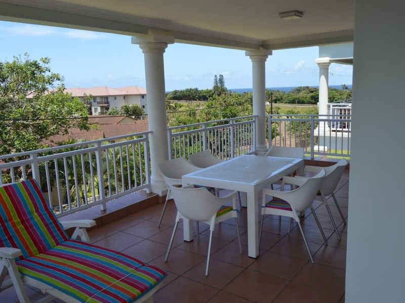 Spacious covered balcony featuring tiled flooring, white metal railings, and structural columns, offering an elevated outdoor living space with scenic views.