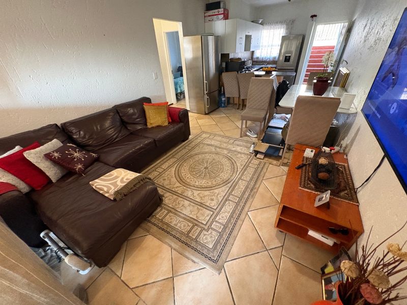 Open-plan living and kitchen area featuring ceramic tiled flooring, functional cabinetry, and direct access to an exterior space via a security gate.