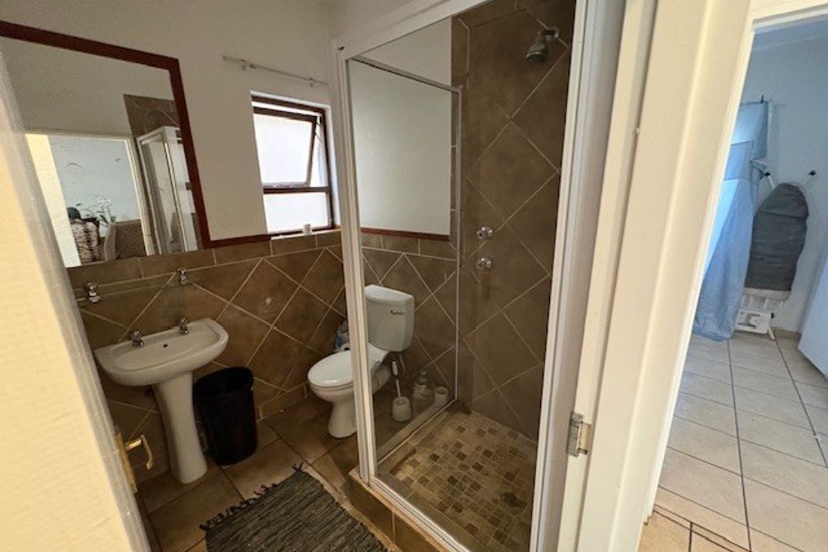 A dated bathroom featuring a pedestal basin, toilet, and a glass-enclosed shower with brown tiled finishes.