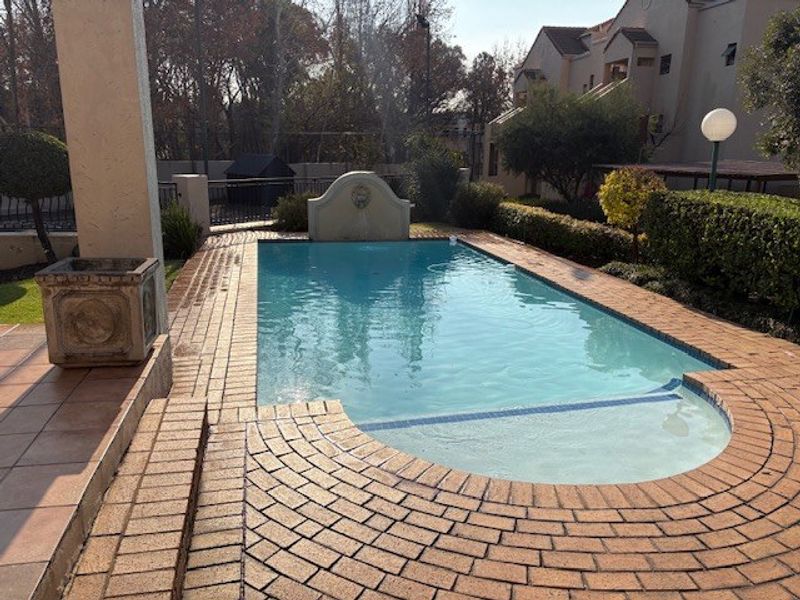 A well-maintained swimming pool area featuring brick paving, a decorative water feature, and established garden landscaping.