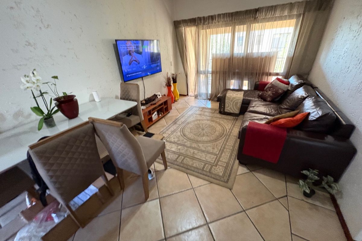 A living room featuring tiled flooring and a sliding glass door leading to an outdoor area, with visible wall surface wear requiring maintenance.