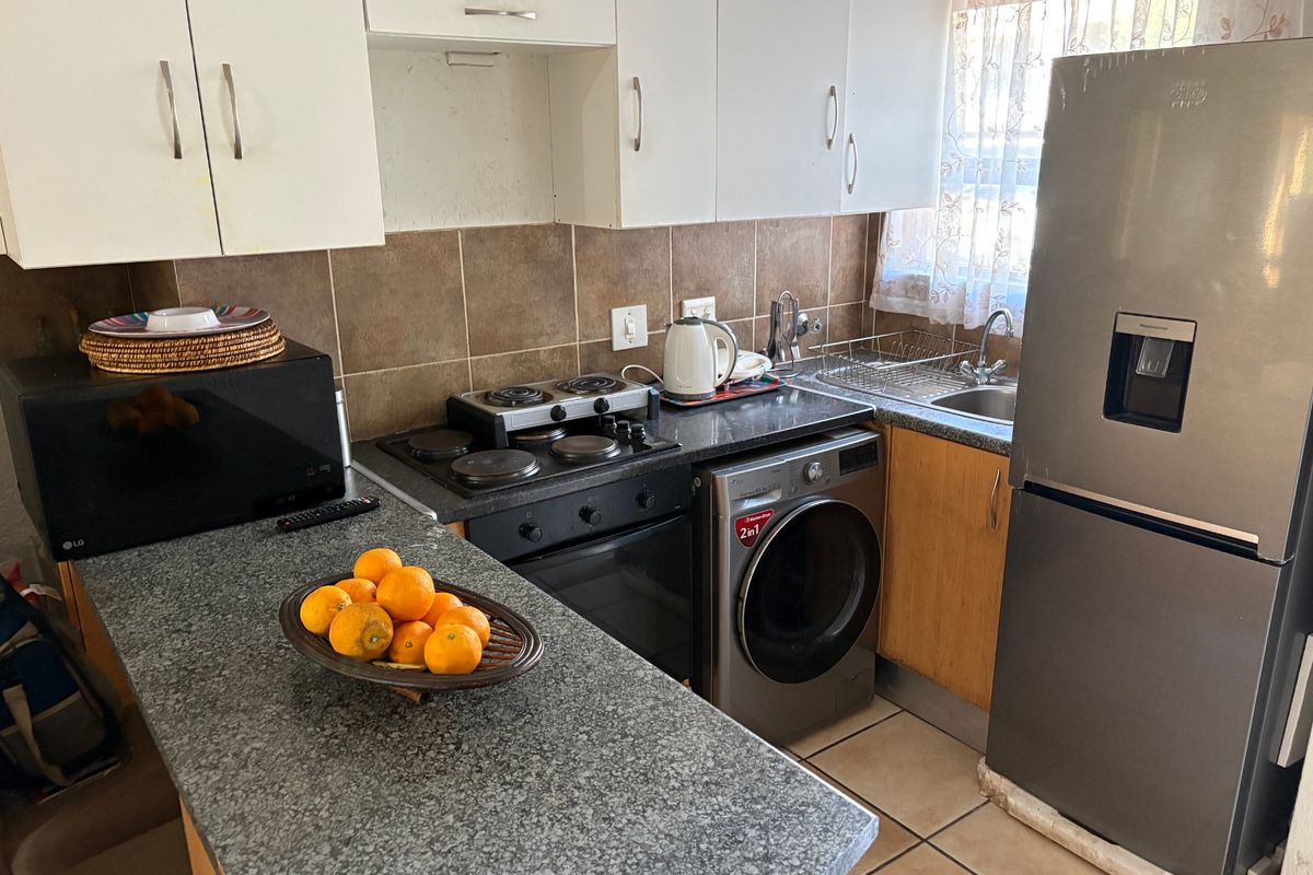 Compact kitchen featuring granite countertops, built-in oven and hob, tiled backsplash, and ample cabinetry, providing a functional workspace for daily meal preparation.