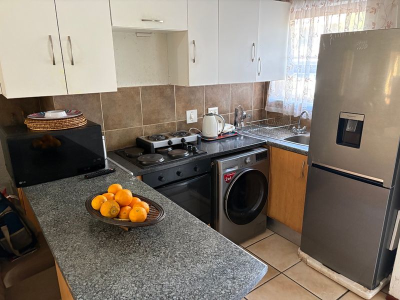 Compact kitchen featuring granite countertops, built-in oven and hob, tiled backsplash, and ample cabinetry, providing a functional workspace for daily meal preparation.