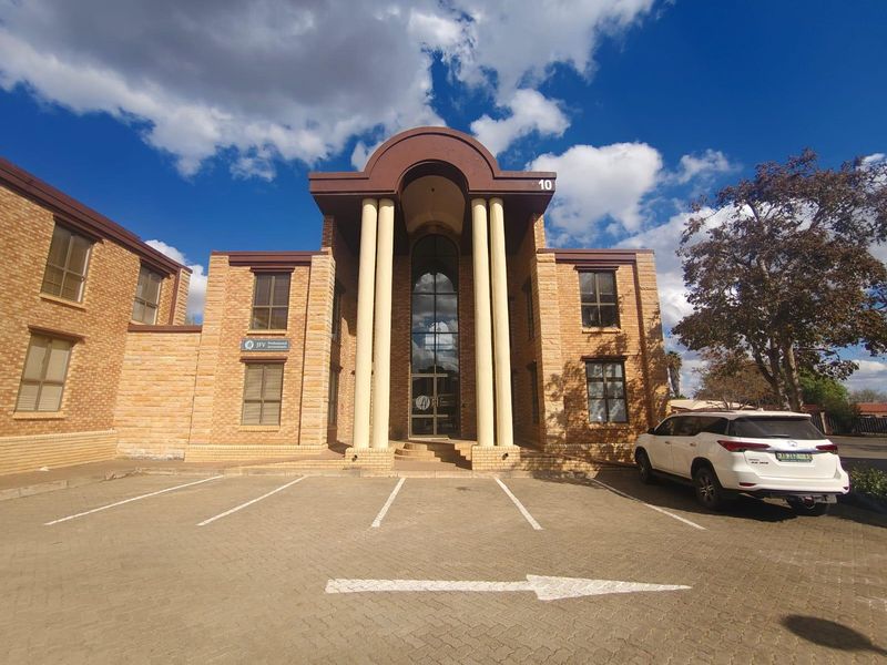Front elevation of a commercial office building featuring a prominent brick facade, decorative columns, and a paved parking area.
