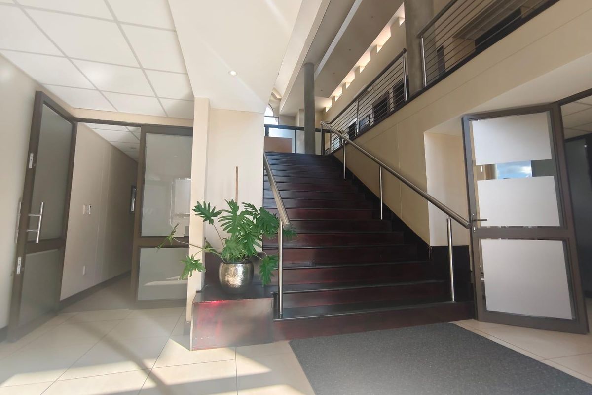 A bright and spacious commercial entrance foyer featuring a prominent wooden staircase with stainless steel handrails, tiled flooring, and access to multiple office areas.